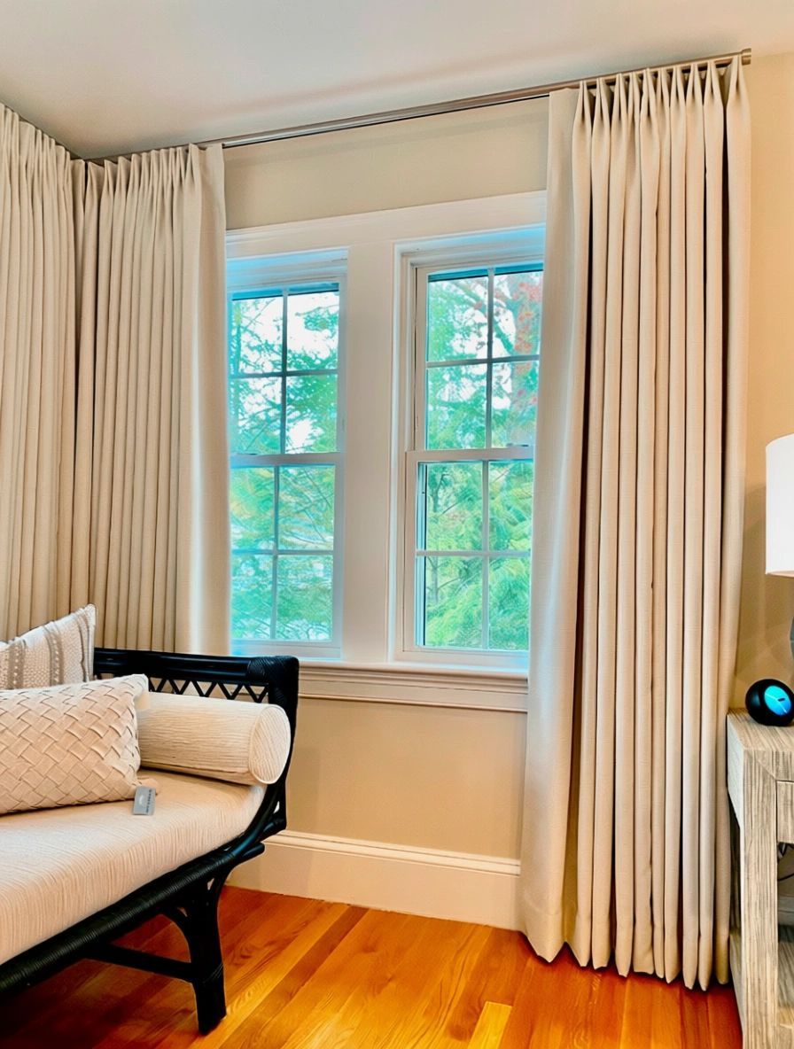 Bright bedroom corner with large window, cream curtains, black daybed, and hardwood floors