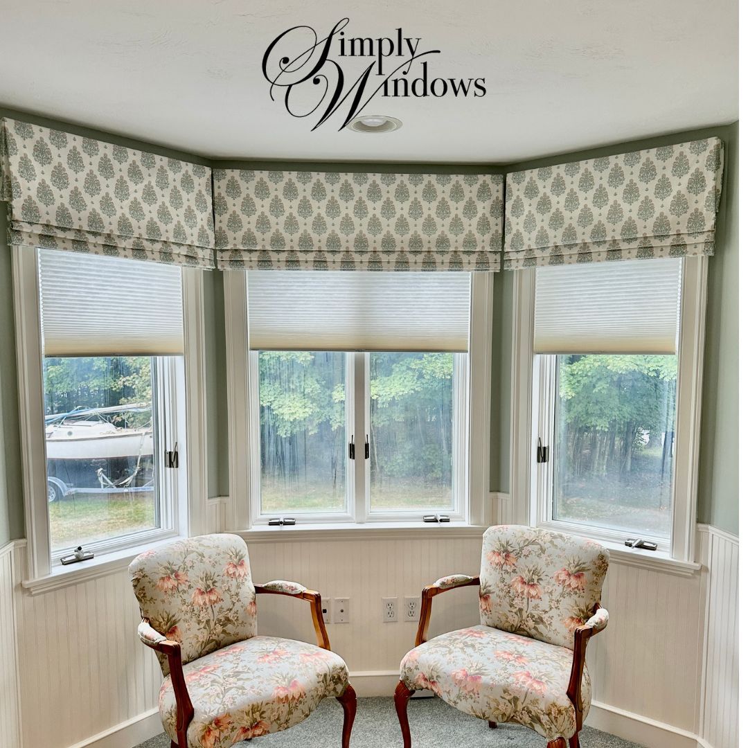 Bay window with floral armchairs, adorned with patterned valances and blinds.