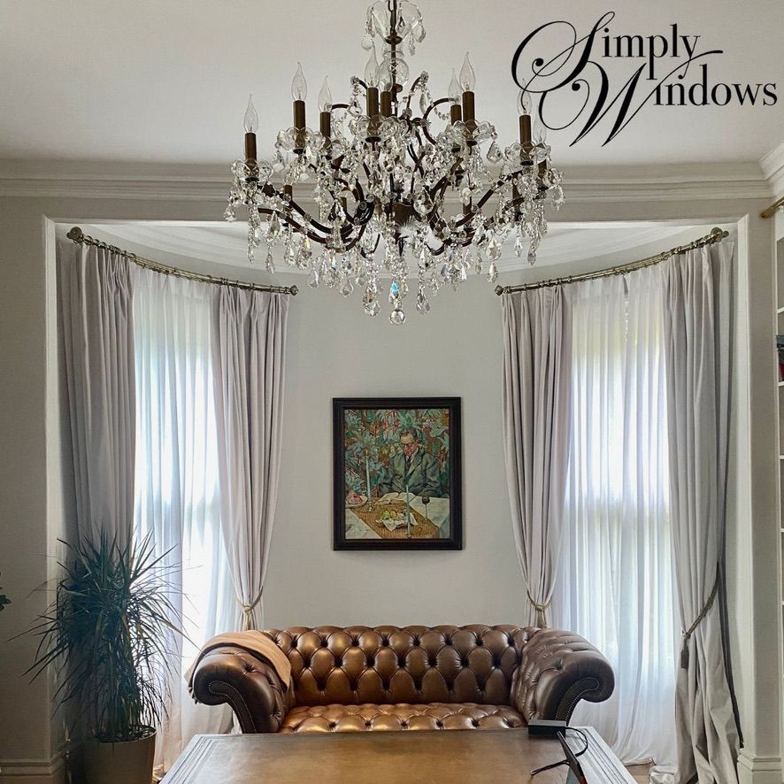 Elegant living room with chandelier, curved bay windows, white curtains, and a brown leather sofa