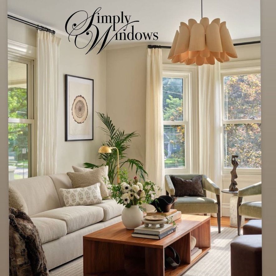 Bright living room with beige drapery,  coffee table, tall windows, and tan pendant lamp.