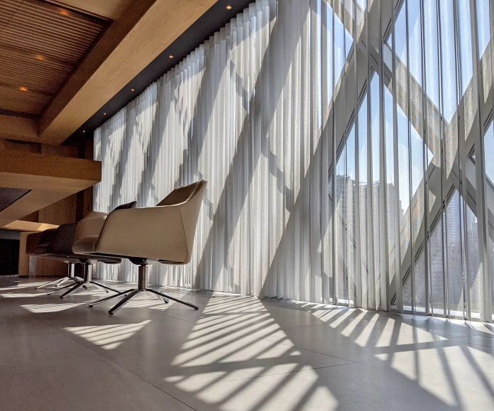 Modern interior with geometric window casting shadow on floor; chairs sit near the window.