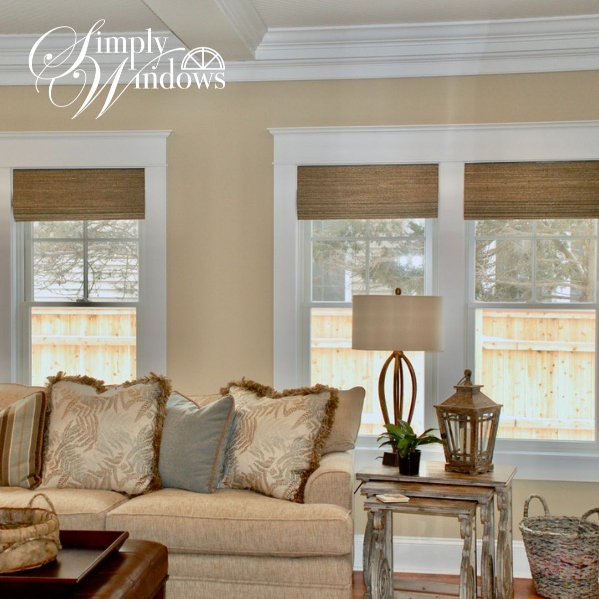 Cozy beige living room with sofa, patterned pillows, woven shades, and white-trimmed windows