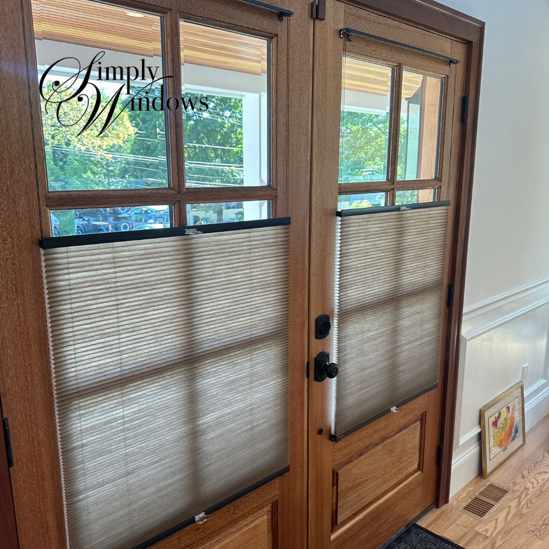 Wooden French doors with woven shades, black hardware, and sunlight from the window above