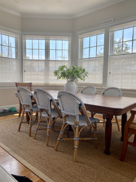 Dining room with table and chairs.  Large windows provide natural light. Beige rug on wood floor.