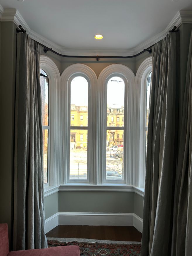 Bay window with arched frames and gray curtains overlooking a city street.