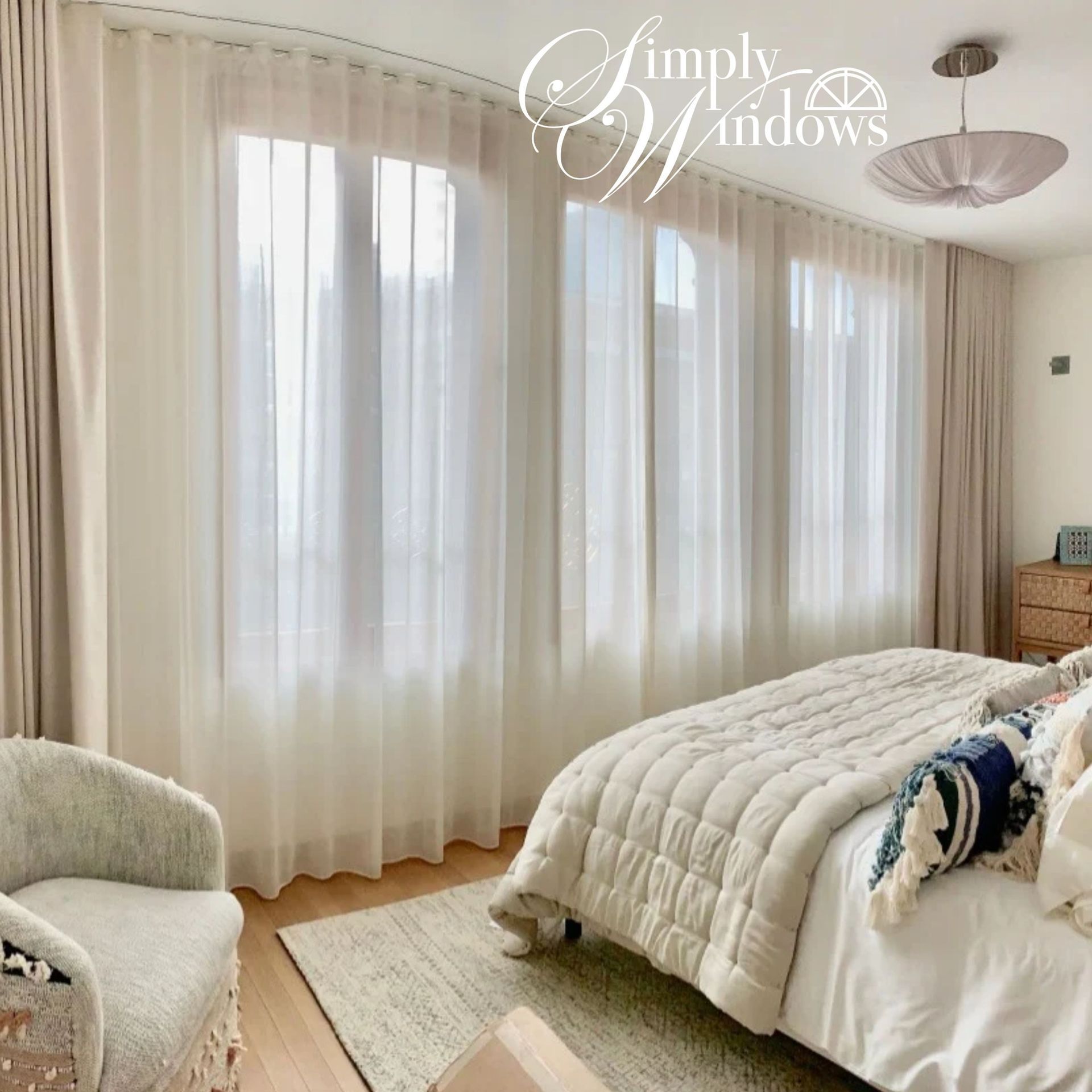 Bright bedroom with sheer curtains, a white bed, armchair, and soft neutral custom drapery.