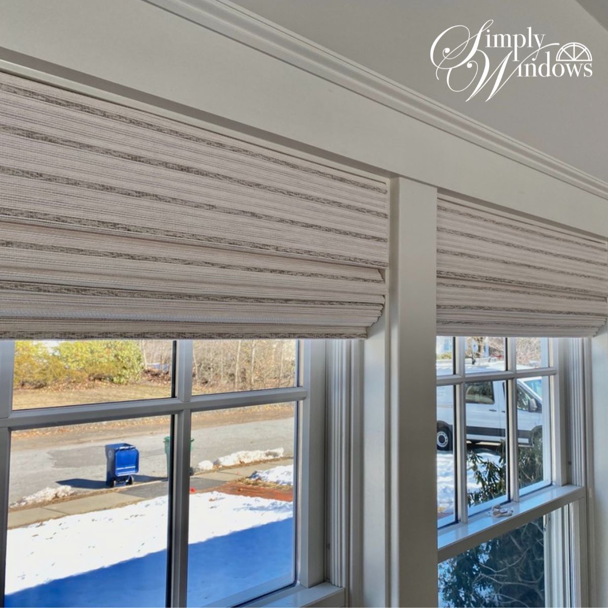Close-up of white striped window roman shades above double windows overlooking a snowy yard.