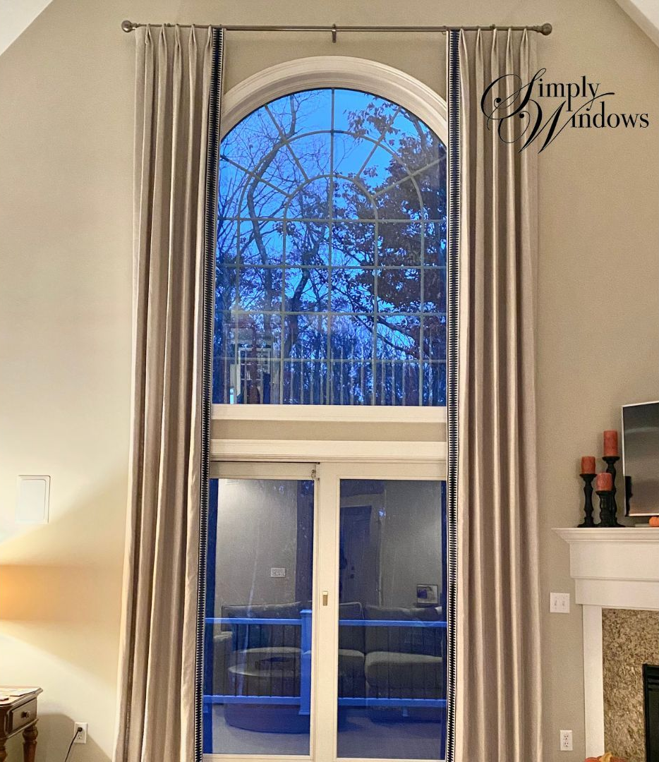 Tall arched window with striped curtains in a beige room, showing patio doors leading outdoors.