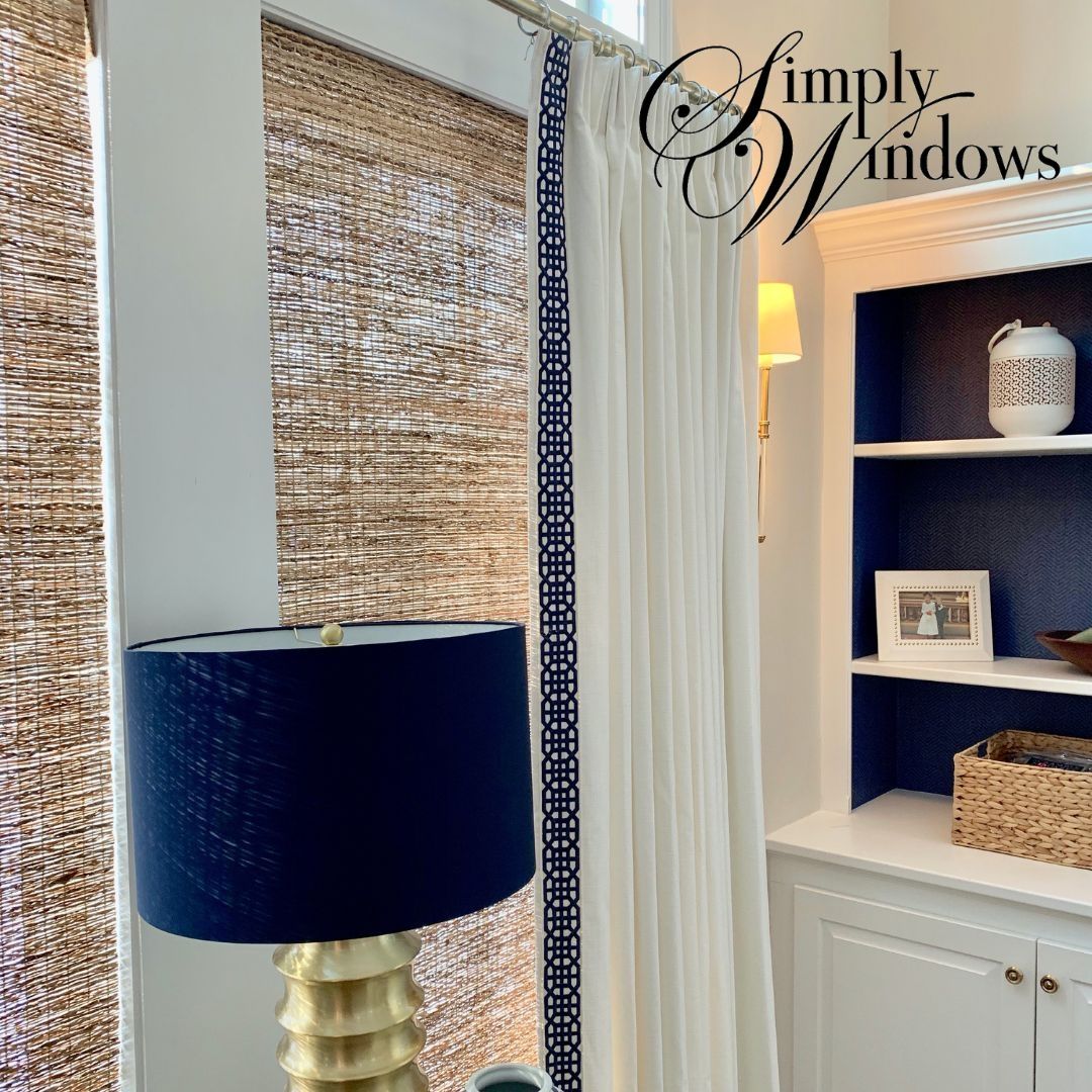 Room with woven wood shades, drapery, a navy lamp, and white built-in shelves with woven baskets.