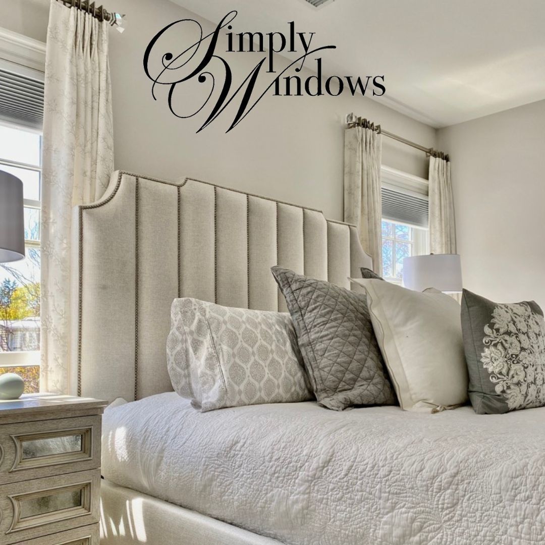 Elegant bedroom with upholstered headboard and layered window treatments with honeycomb shades and drapery. 