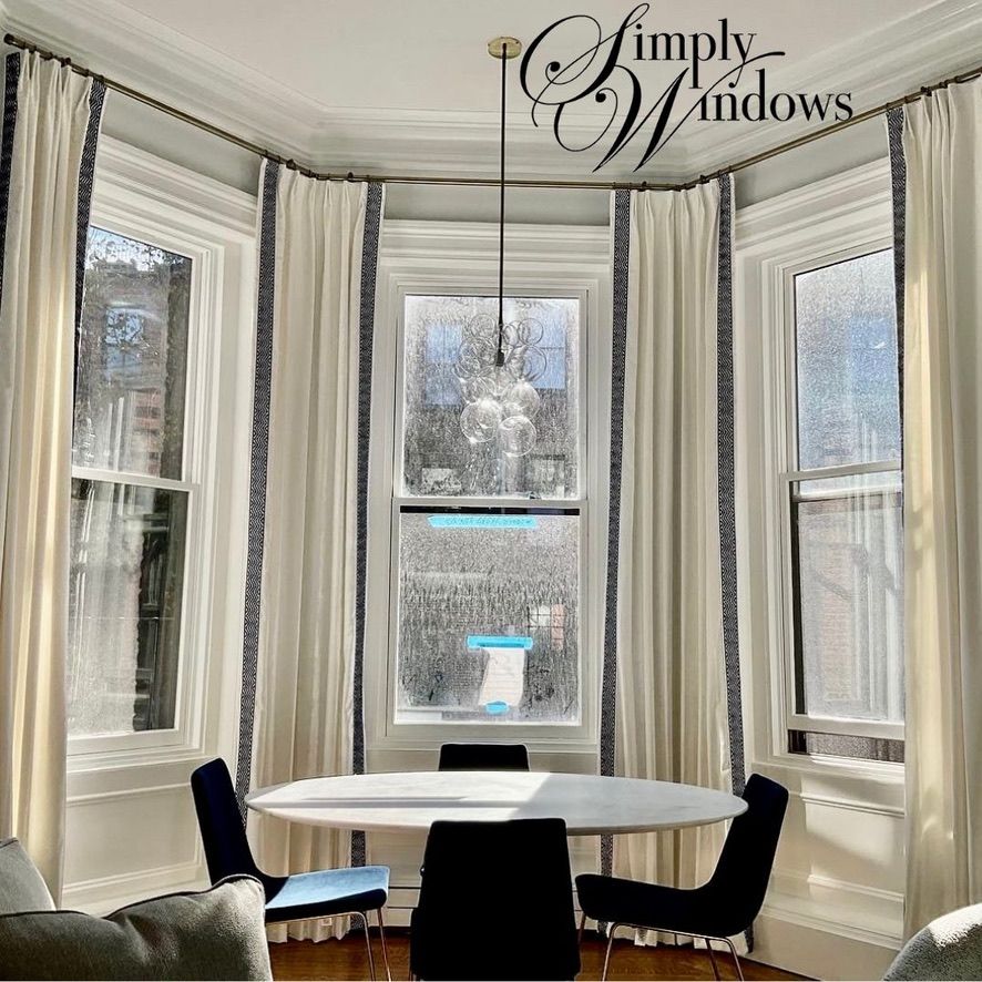 Bright dining nook with bay windows, custom drapery, and a round white table with black chairs