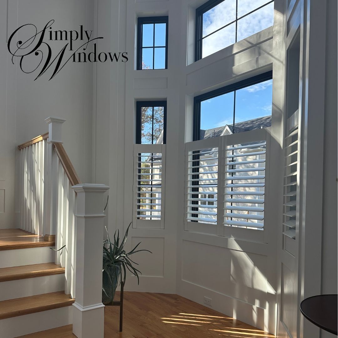 Sunlit staircase and bay windows in a bright white entryway with hardwood floors and shutters