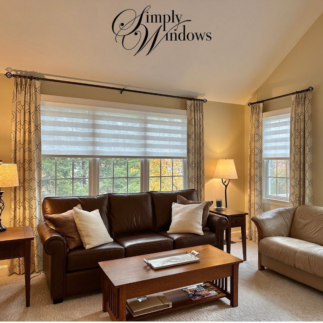Cozy living room with brown leather sofa, and large windows with layred window treatments.