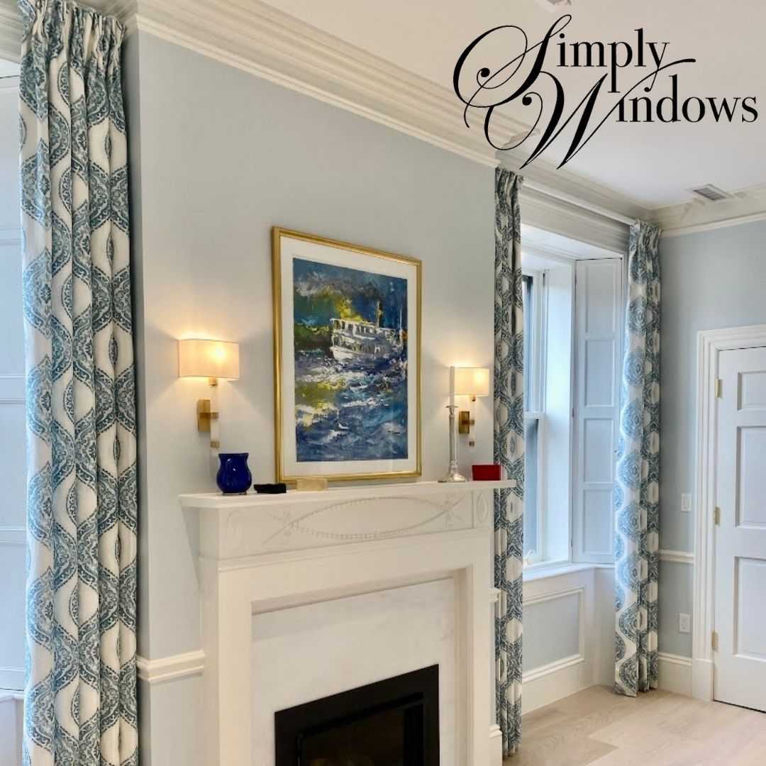 Elegant living room with blue patterned drapery, white fireplace, and framed coastal painting