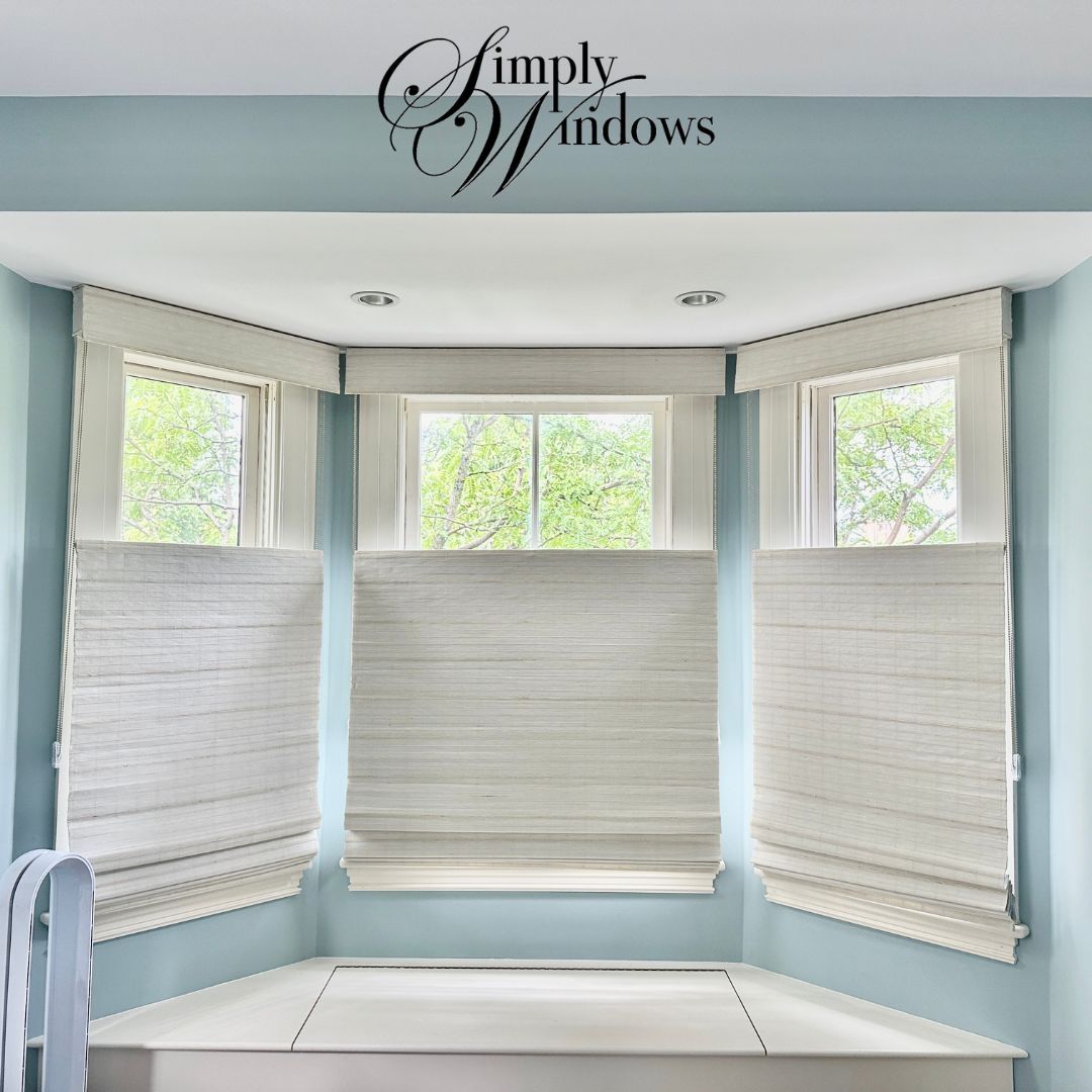 Bright bay window with white Roman shades in a light blue room