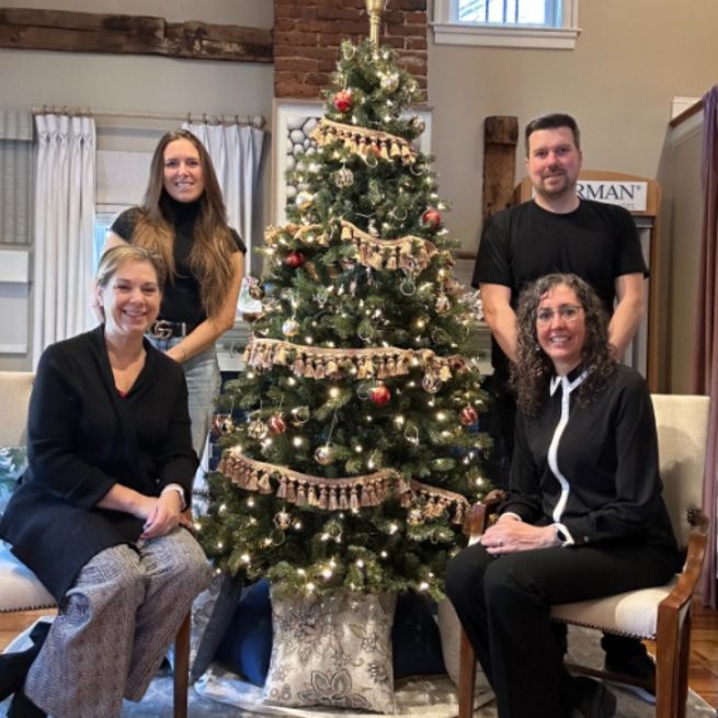 Five people pose in front of a decorated Christmas tree in a room with a brick wall and curtains.
