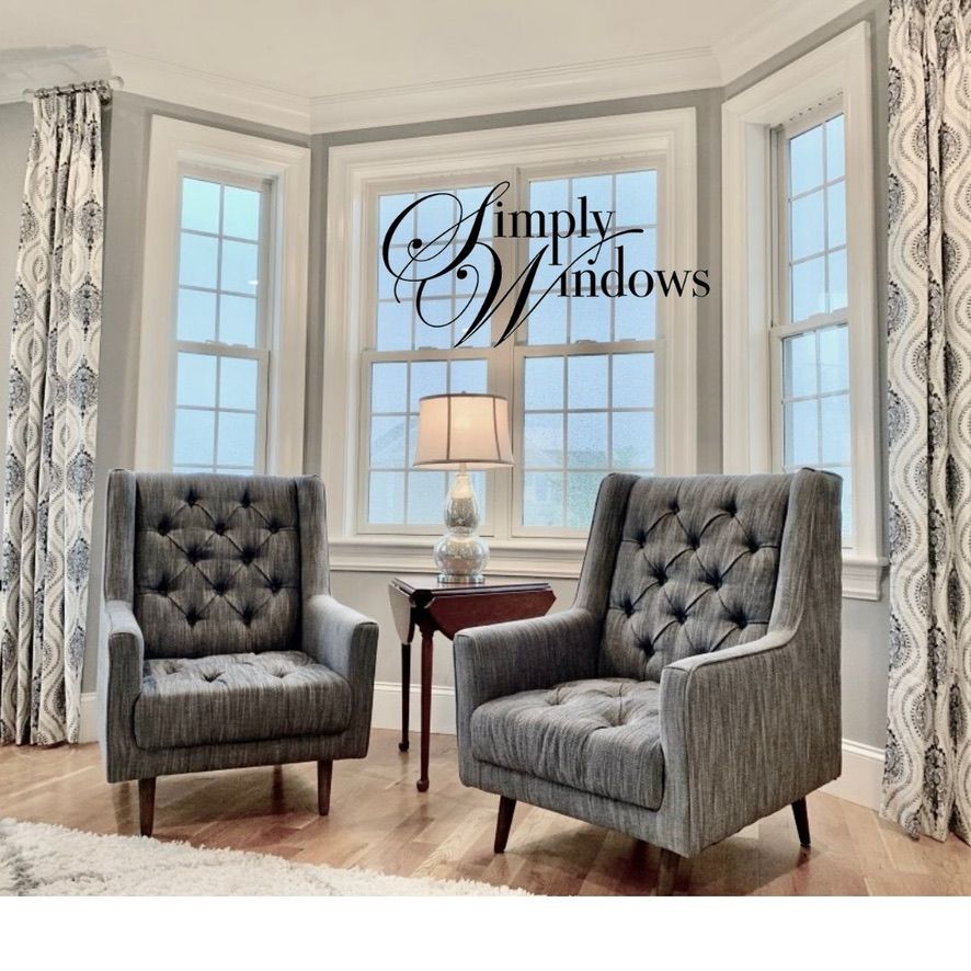Elegant gray chairs and a small lamp in front of a bay window with draped curtains, labeled “Simply Windows.”
