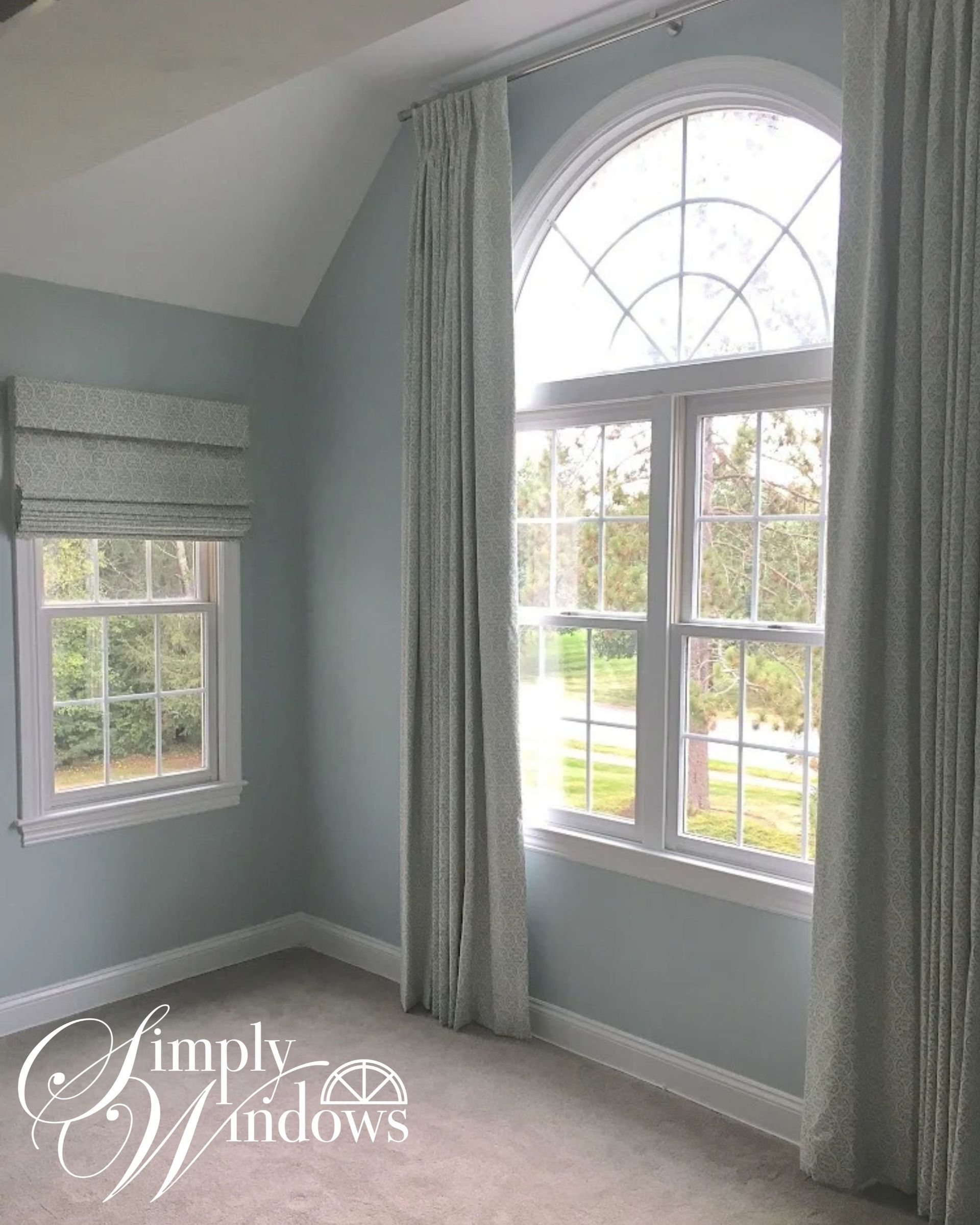 Bright bedroom with large arched window, gray drapery, and soft blue walls.