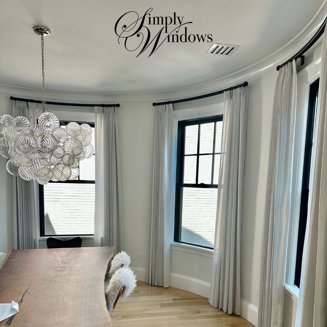Curved bay-window dining room with white drapery, crystal chandelier, and round wood table