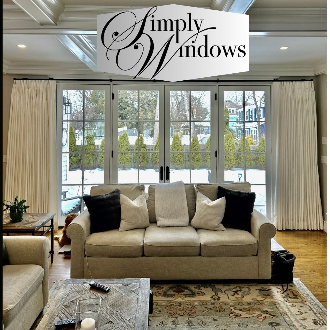 Living room with light-colored sofa, windows with white drapes, and a Simply Windows logo.