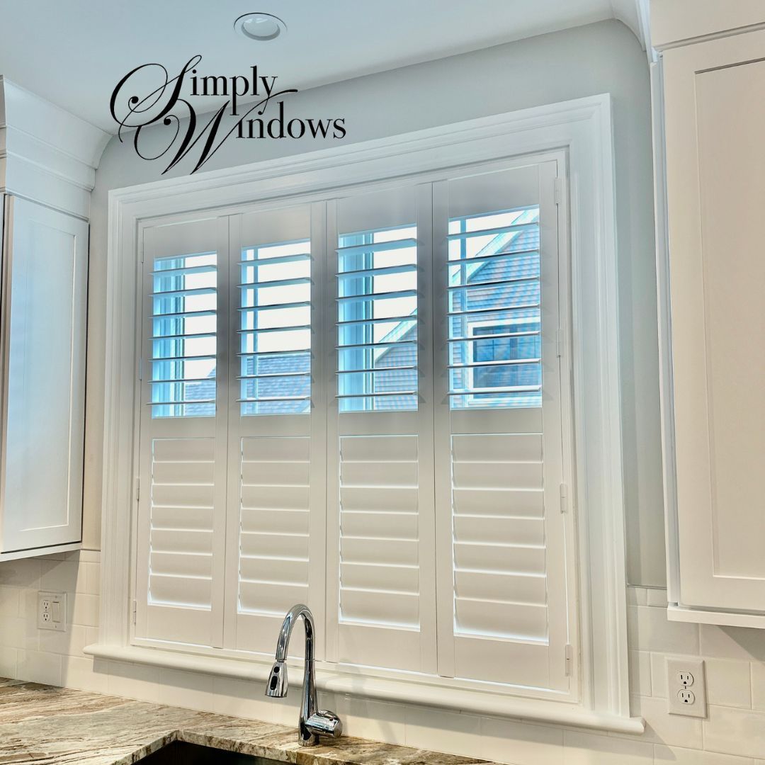 White kitchen window with plantation shutters above a sink and chrome faucet, blue sky visible outside
