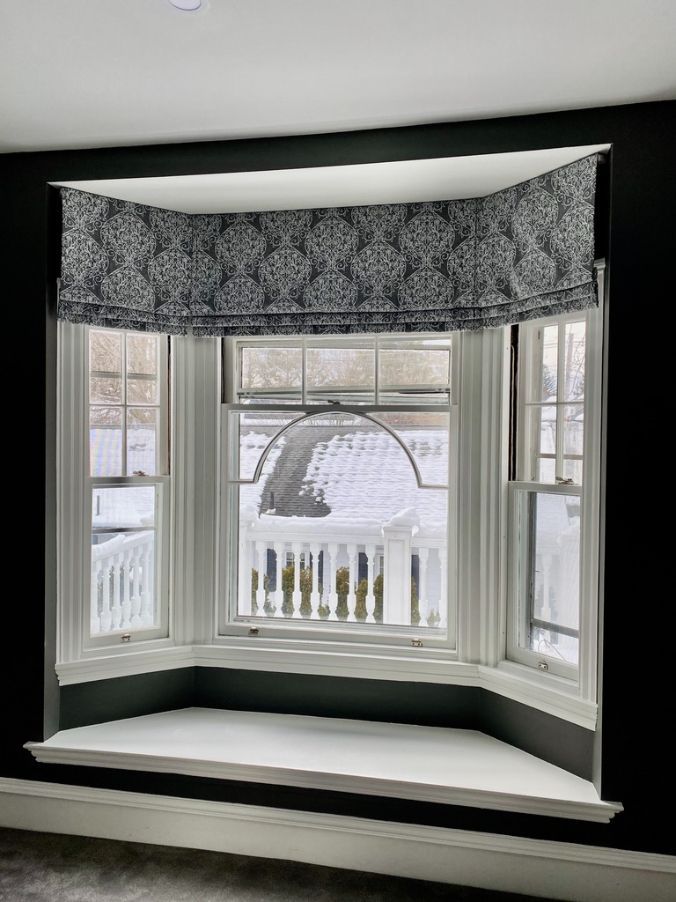 there is a window seat in front of a bay window with roman shade window treatments Simply Windows.