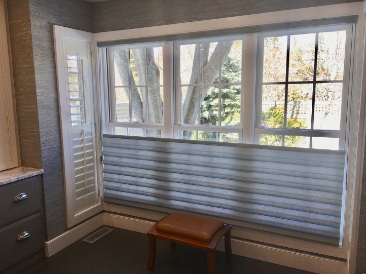 a room with a large window and a bench in front of it and window treatments .
