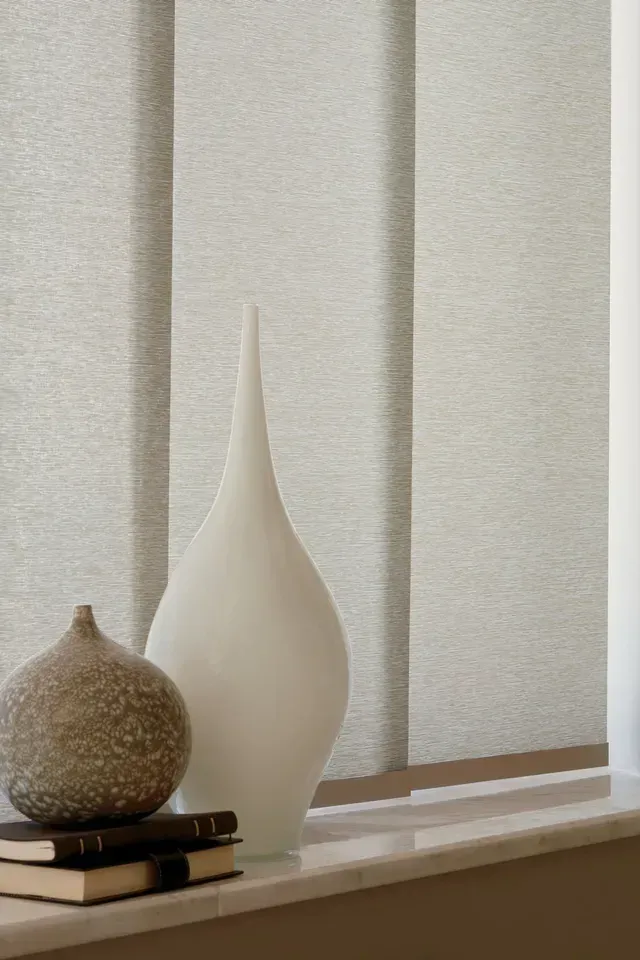 Window sill with books, two white vases, and light-colored vertical blinds.