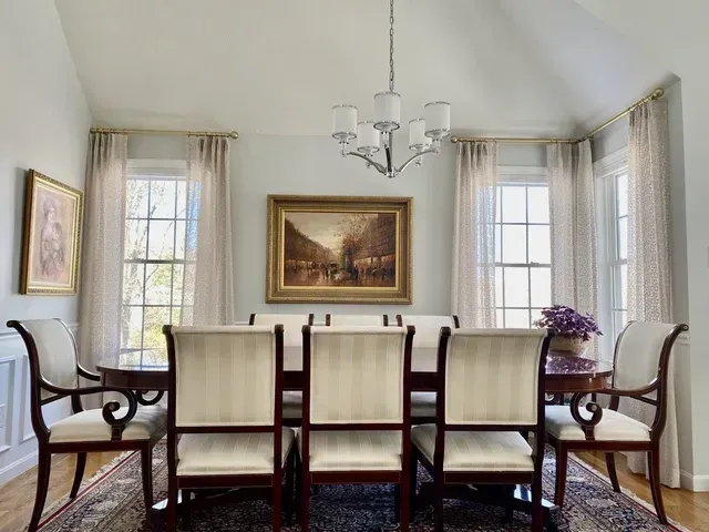 Elegant dining room with chandelier, oval table set for eight, artwork, and windowed walls.