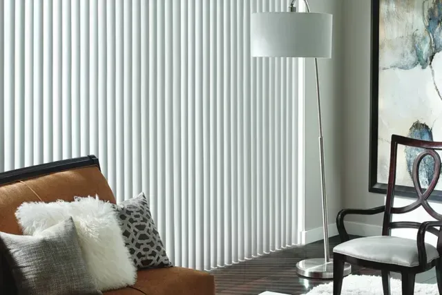 Living room with vertical blinds, chair, floor lamp, and artwork. Brown couch with pillows.