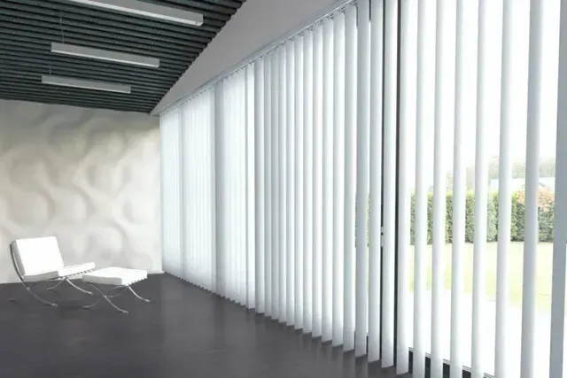 Modern room with white vertical blinds, white chair, textured wall, and dark floor.