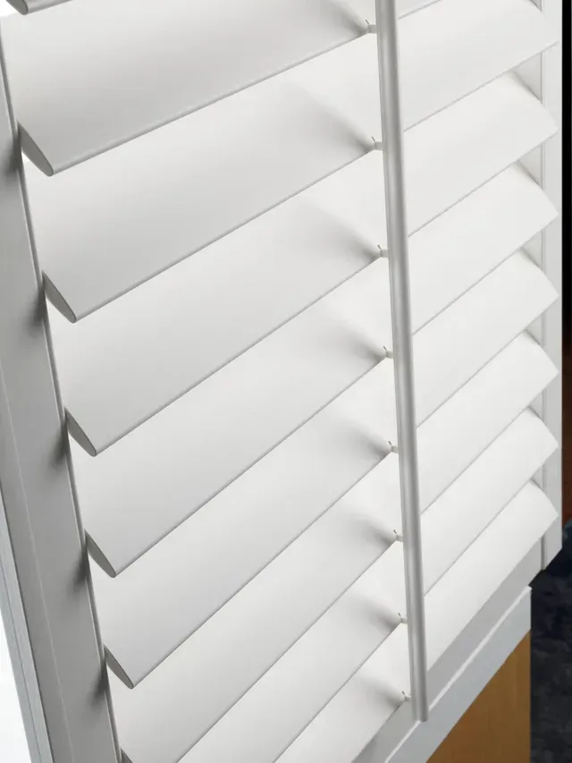 White plantation shutters, closed, angled slats. Vertical rod runs through the center.