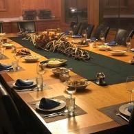 Long conference table set for a formal meeting, with plates, glasses, napkins, and a floral centerpiece.