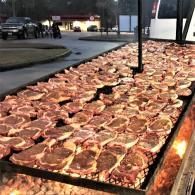 Rows of marinated steaks sizzling on a large outdoor grill at night