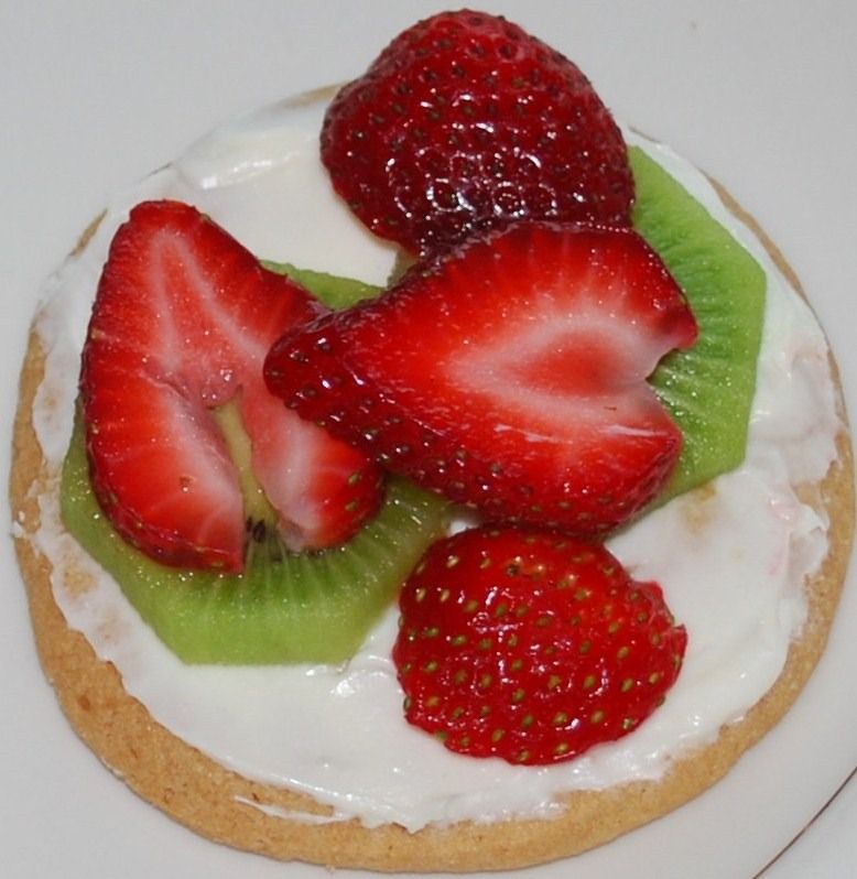 Strawberry tart topped with whipped cream, kiwi slices, and fresh strawberry halves on a white plate