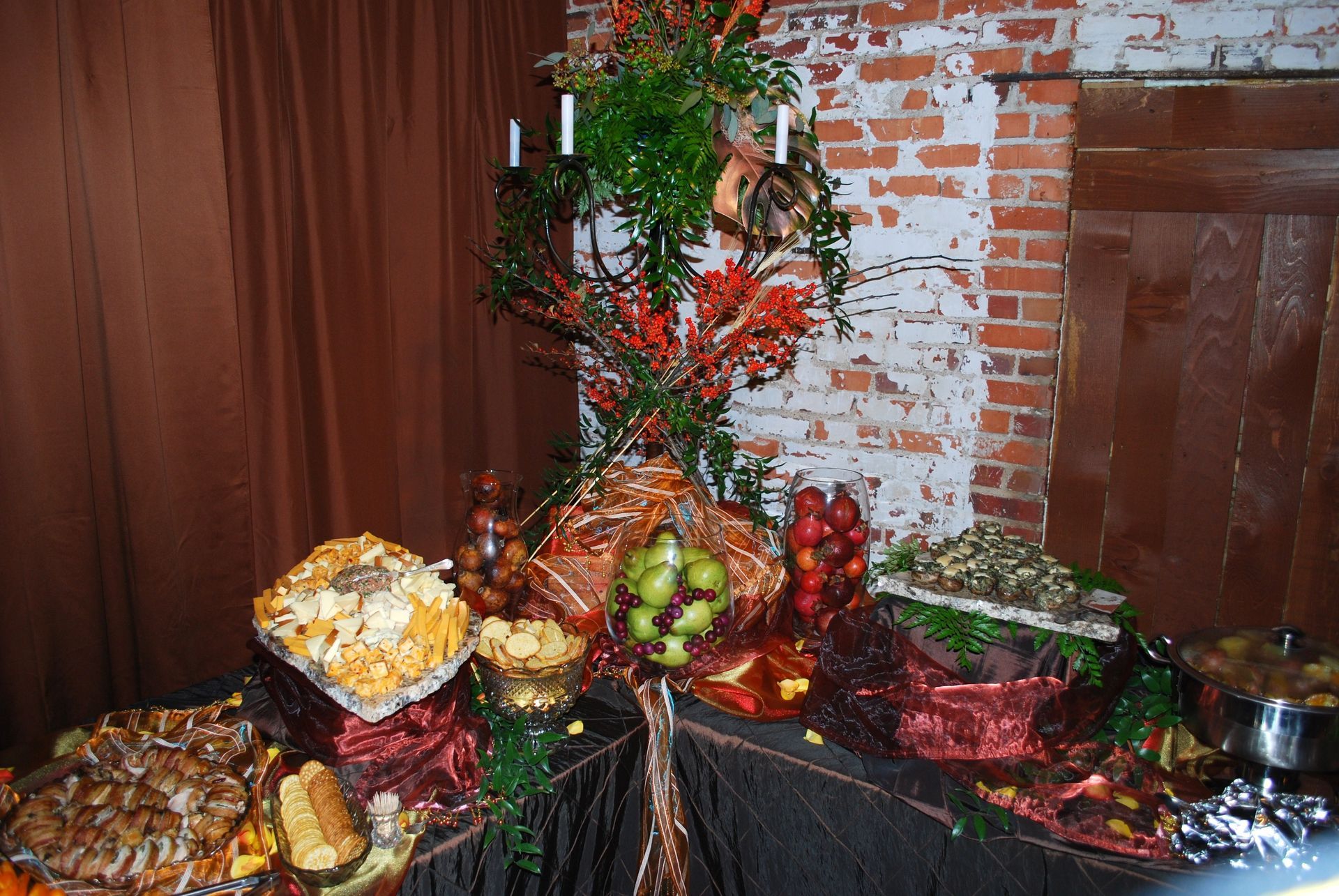 Decorative autumn centerpiece with fruit, flowers, and greenery on a table beside a brick wall