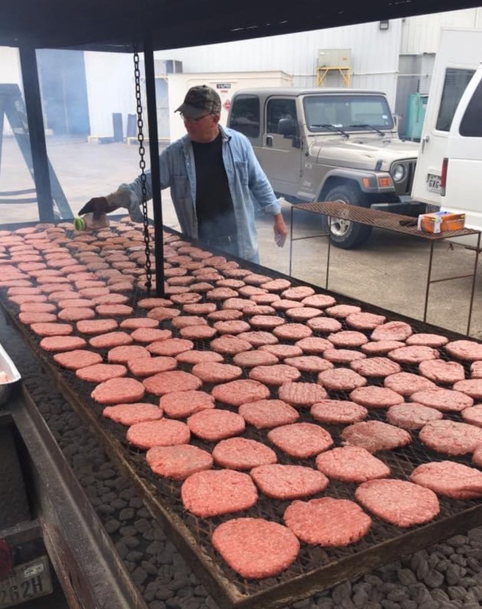 Man grilling rows of burger patties on a large outdoor flat-top grill under a canopy