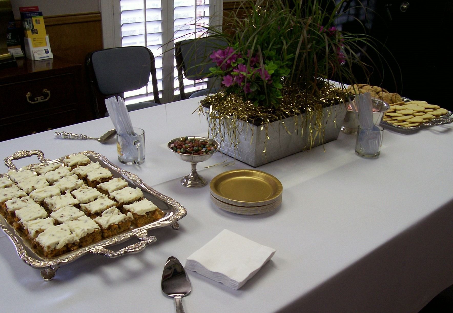 Buffet table with frosted pastries, gold plates, utensils, and a flower centerpiece