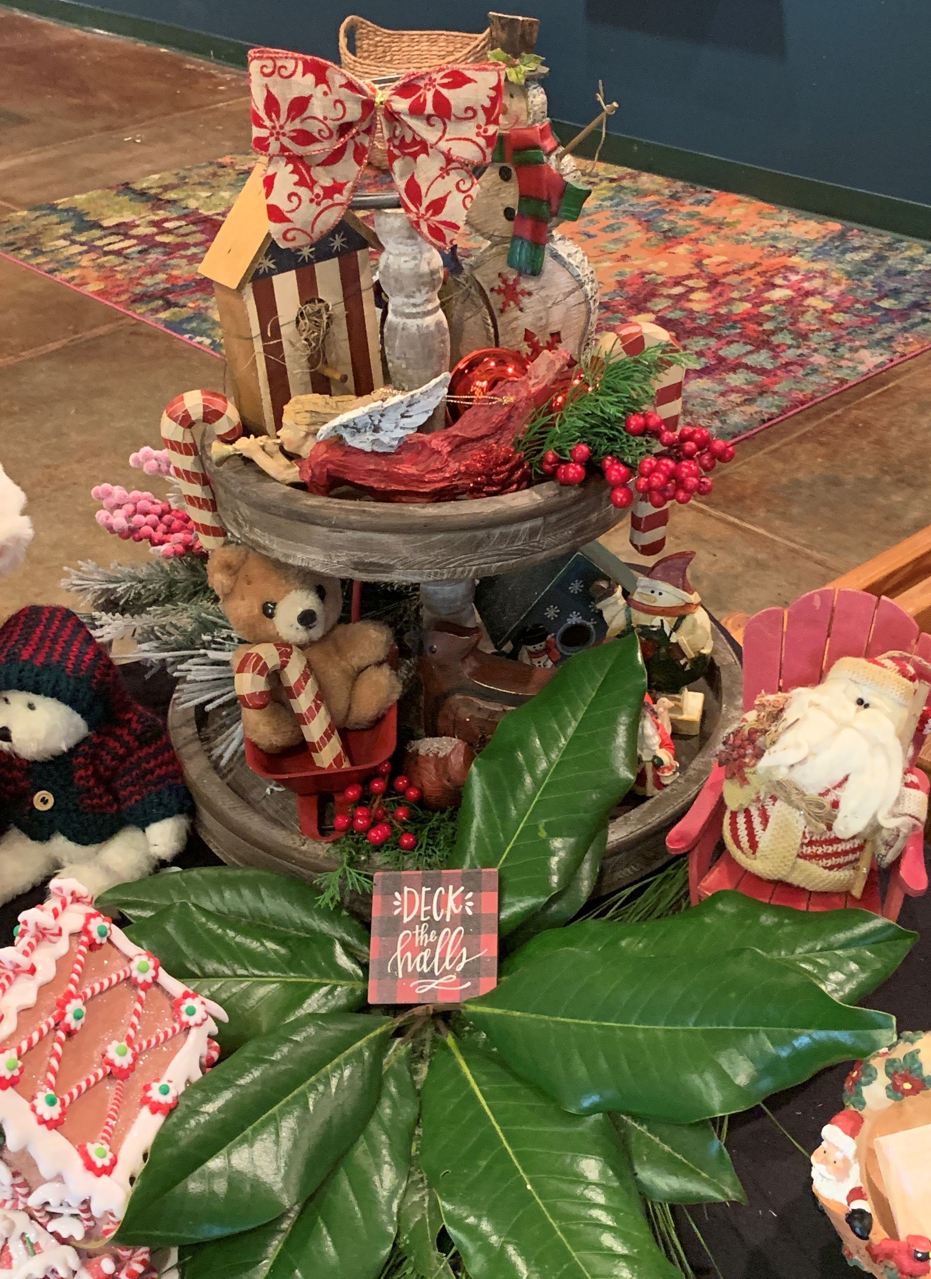 Festive holiday tabletop display with teddy bears, Santa figures, red berries, and a wrapped gift centerpiece
