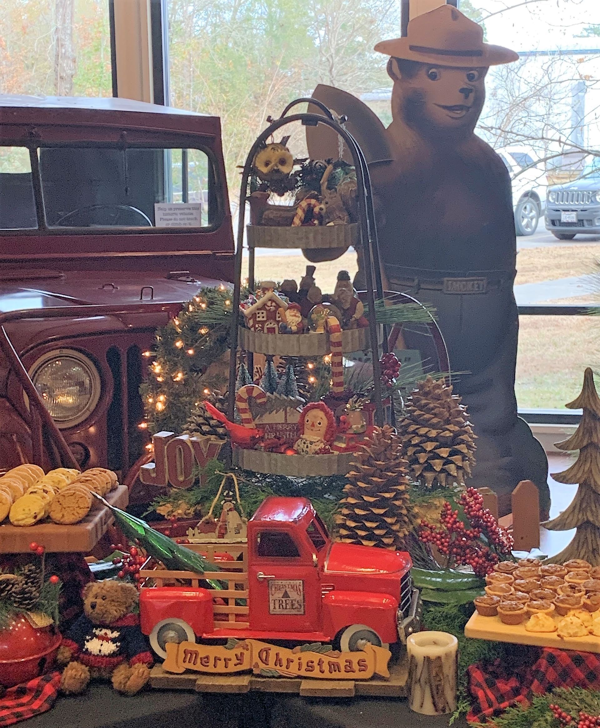 Rustic holiday display with a red truck, pinecones, and Christmas decorations beside a mannequin in a hat.