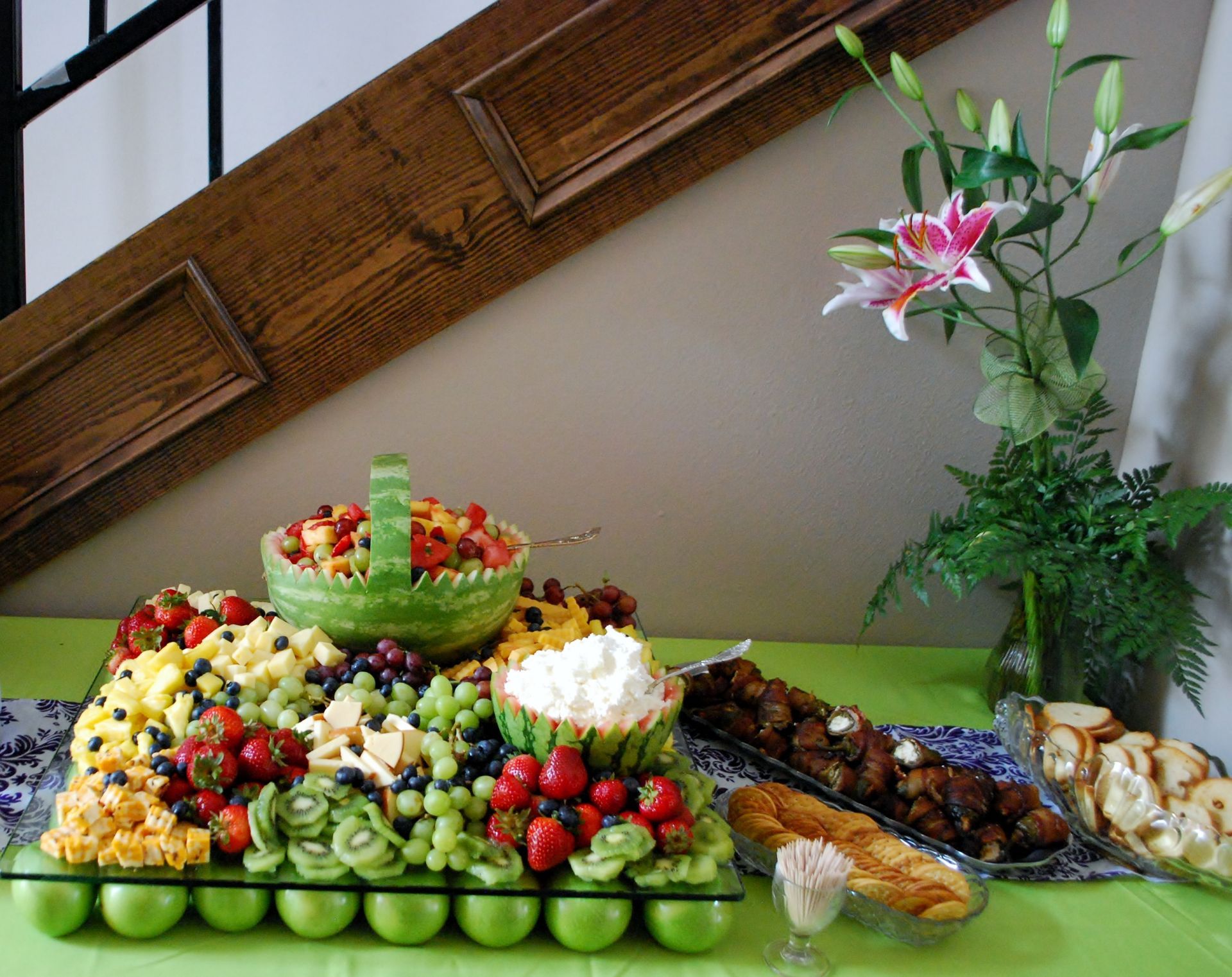 Colorful fruit and dessert buffet on a green table with flowers and assorted platters