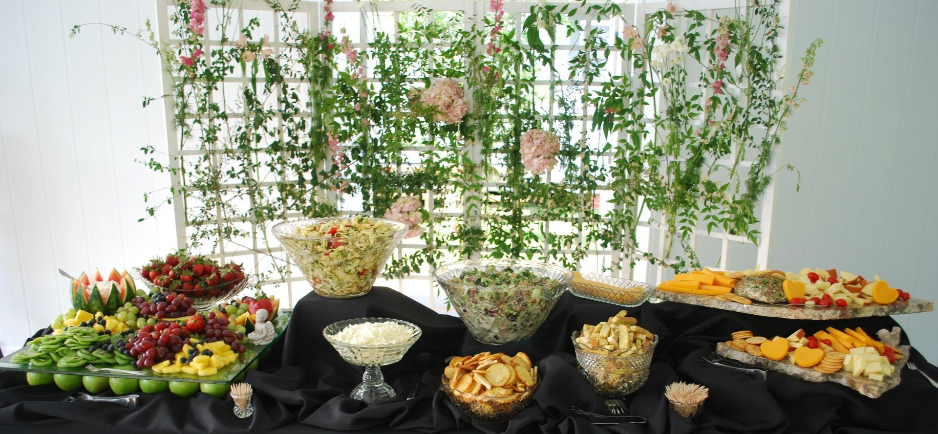 Buffet table with fruit, pastries, and dessert platters in front of a decorative floral backdrop