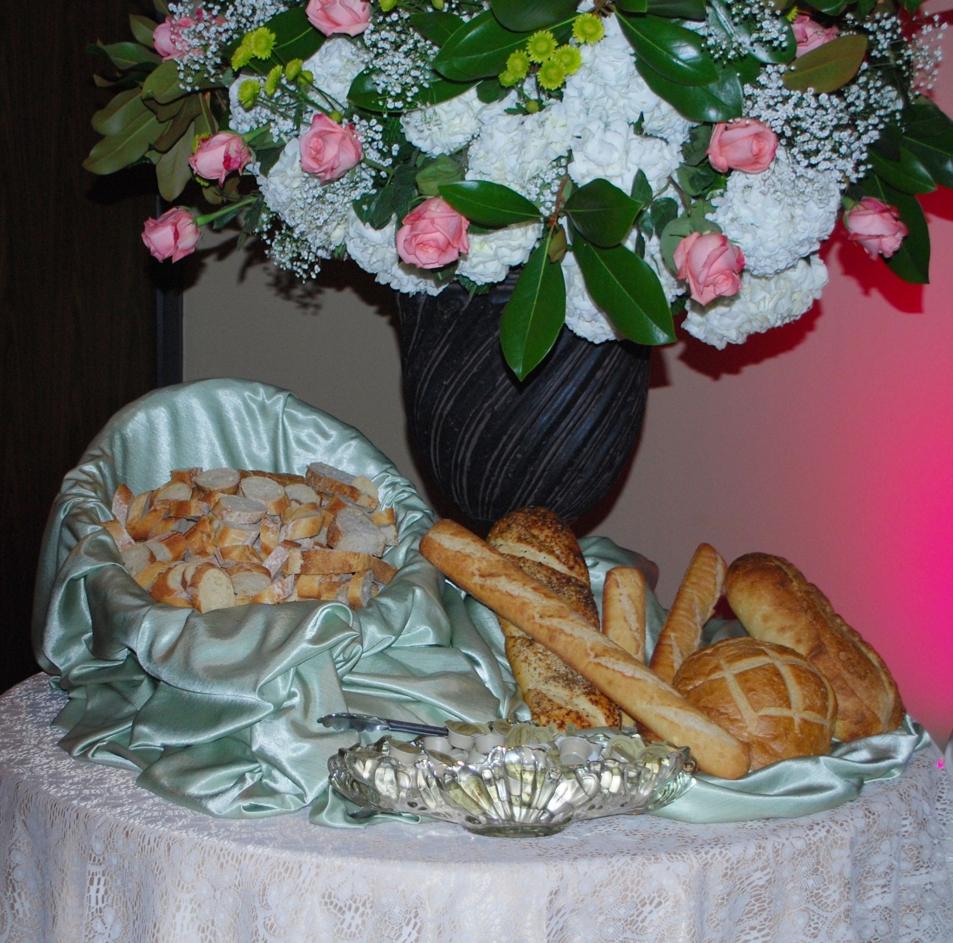 Floral centerpiece above a lace-covered table with bread, pastries, and a silver tray of fish