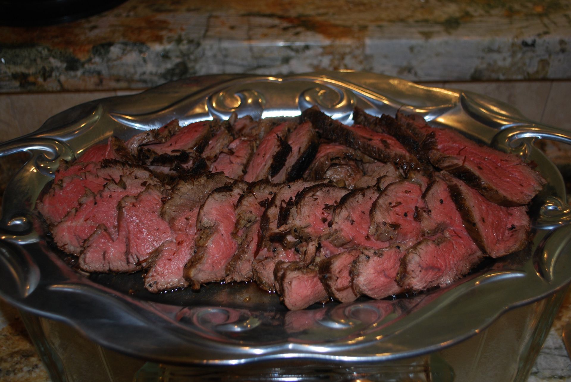Thinly sliced roast beef on a silver platter, drizzled with dark sauce.