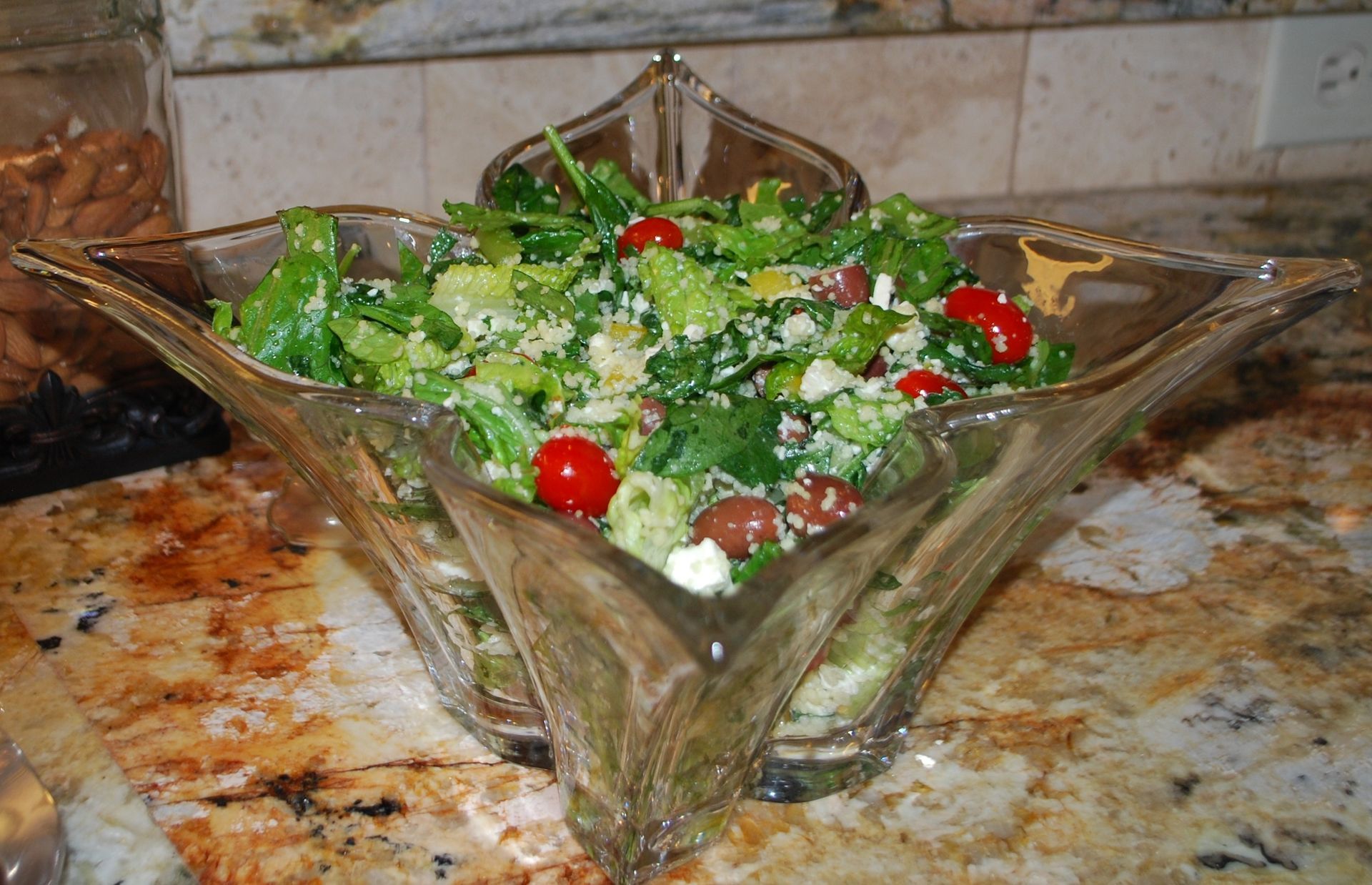 Glass bowl of green salad with cherry tomatoes and cheese on a kitchen countertop