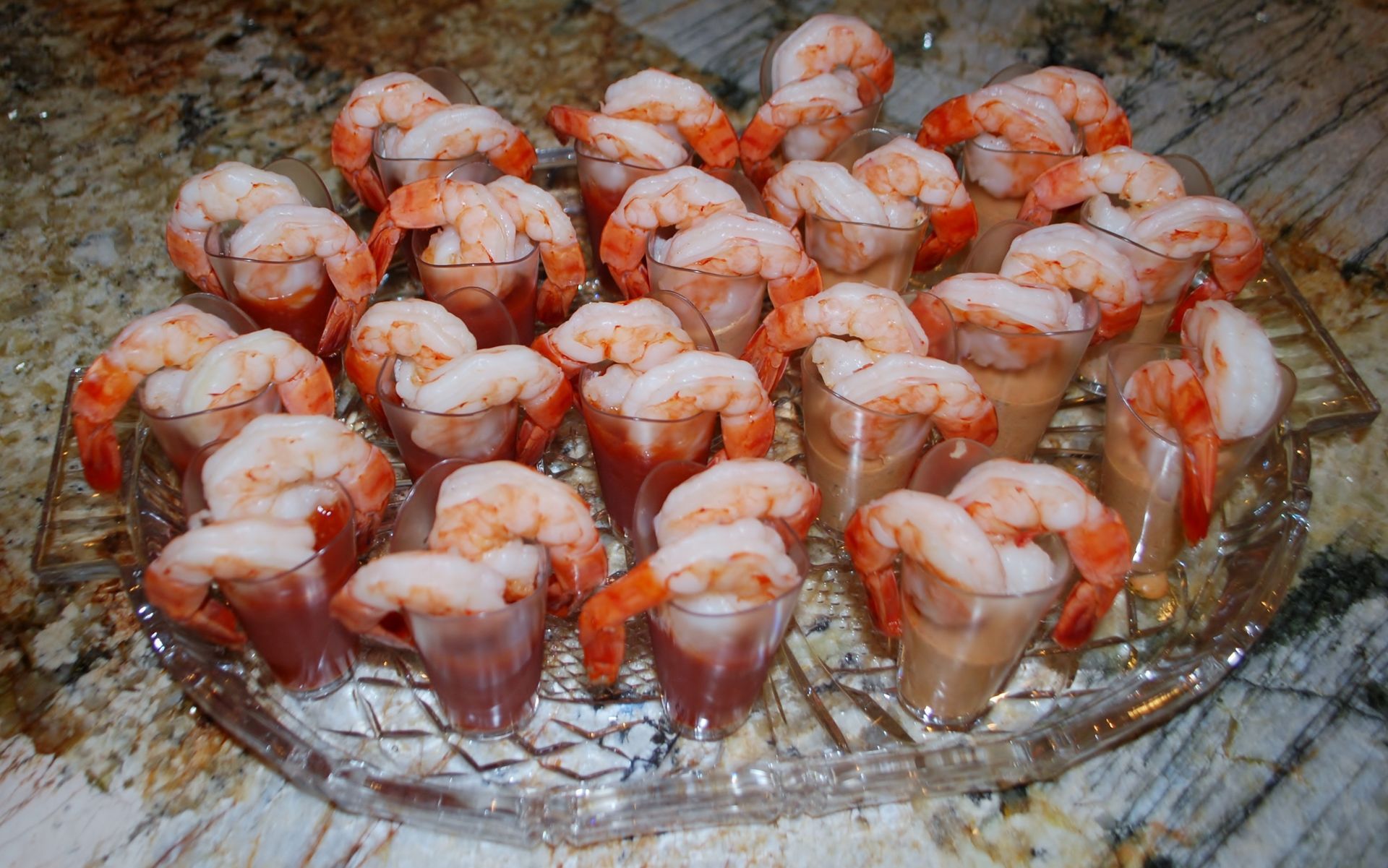 Tray of shrimp cocktail appetizers on a glass platter, topped with red sauce.
