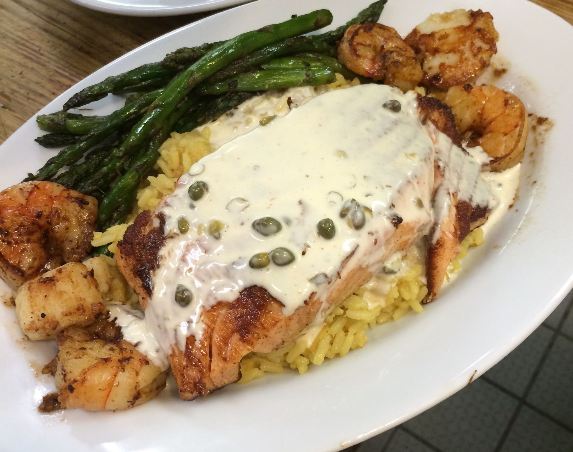 Seared fish with creamy sauce, rice, asparagus, and roasted potatoes on a white plate