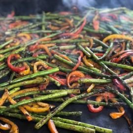Grilled mixed chili peppers sizzling on a hot pan, with smoke rising and charred green, red, and yellow peppers