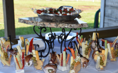 Dessert display with small glasses of layered treats and berries on a metal stand at a table outdoors.