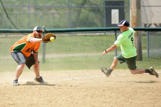 A person wearing a hat and orange shirt, holding a baseball bat on their shoulder on a baseball field.